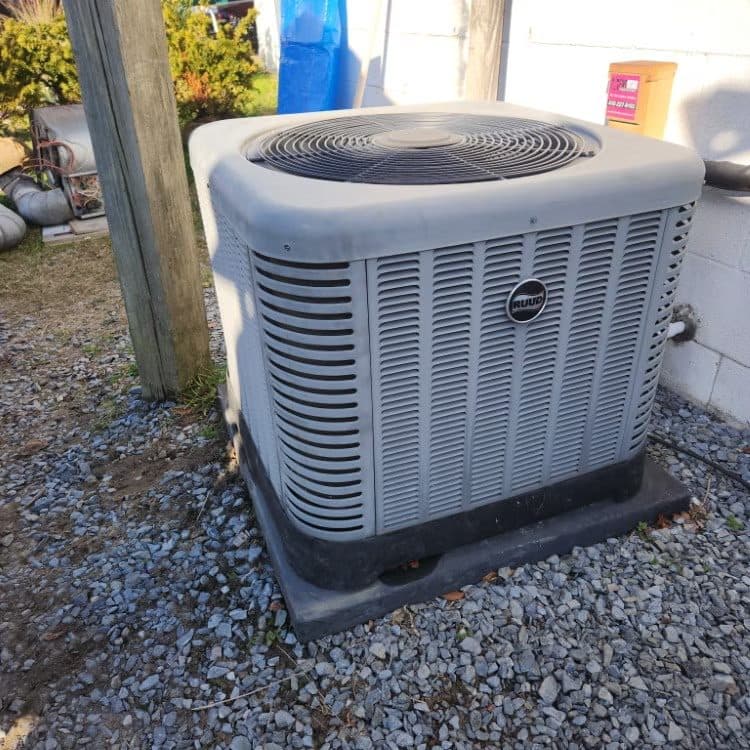 New heat pump condenser installed on a gravel bed with composite pad at a rural home