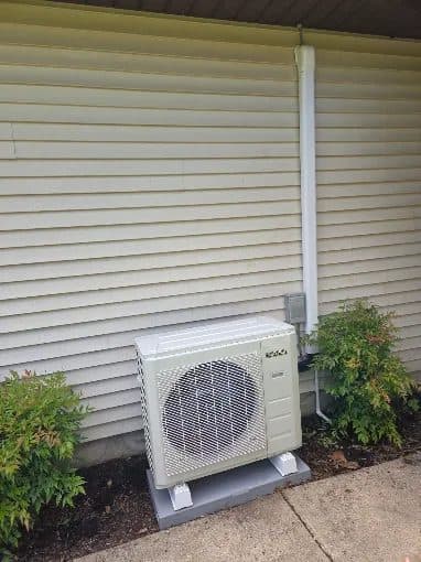 Mini-split outdoor condenser on a pad with line-hide cover running up vinyl siding