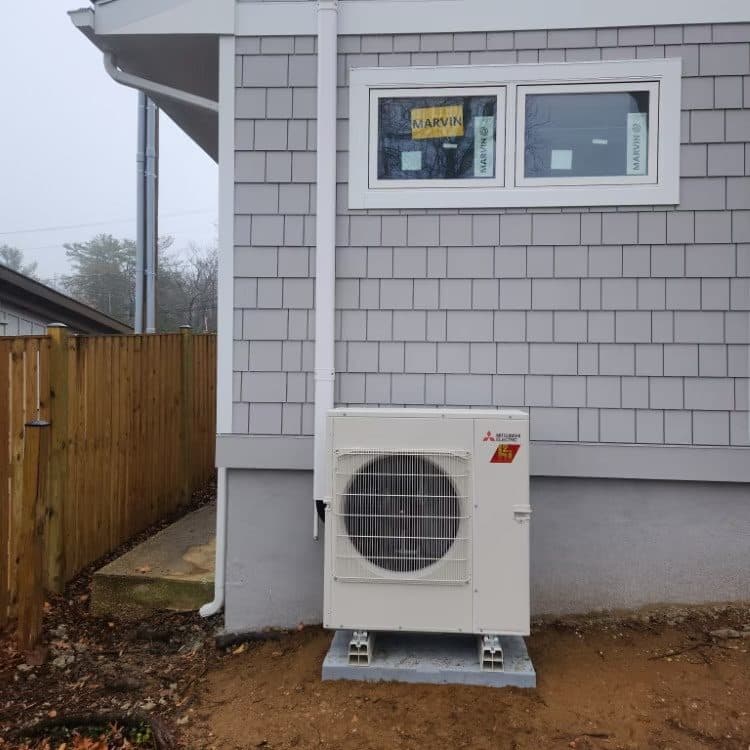 Mitsubishi hyper-heat outdoor unit installed on a pad beside a shingle-sided cottage
