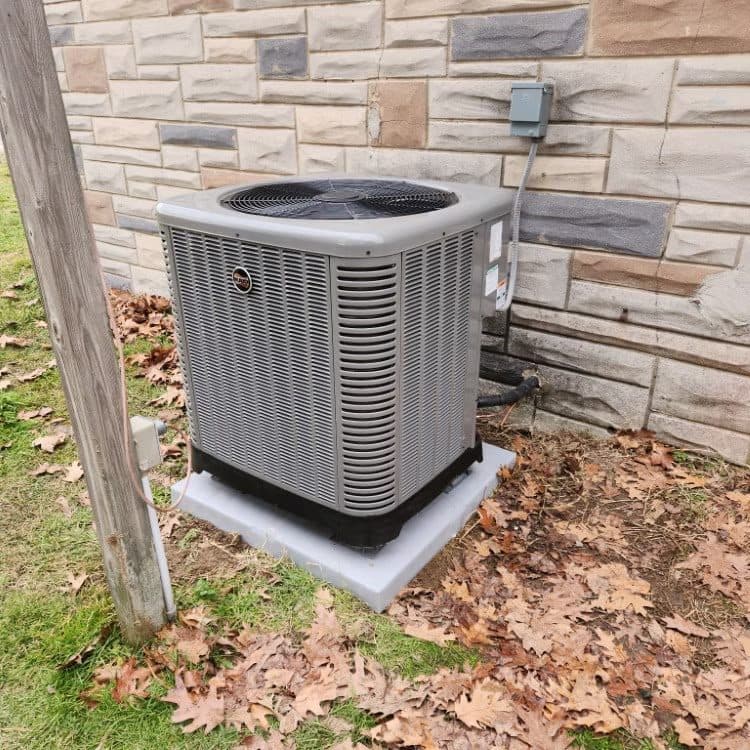 Rheem heat pump installed on a pad against a stone veneer foundation