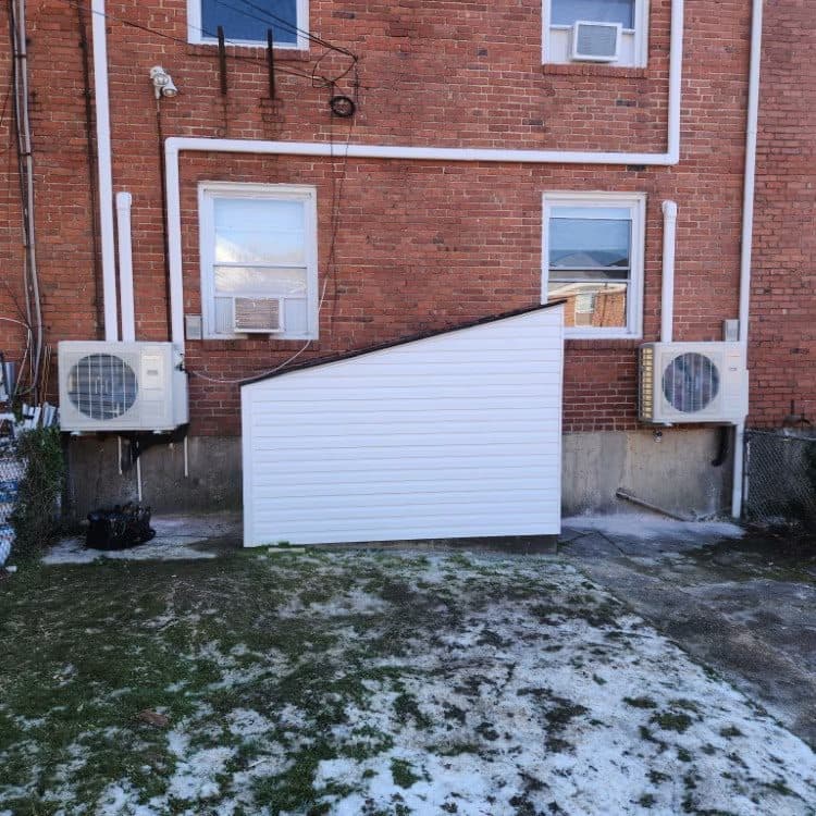 Two ductless mini-split outdoor units installed at the rear of a brick home in winter